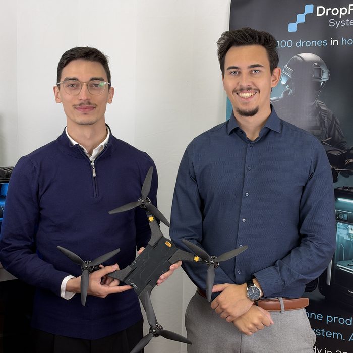 Die beiden DropForce-Gründer halten eine STURM 01 Drohne, dahinter eine Druckeinheit des Tactical Case und das DropForce-Banner.