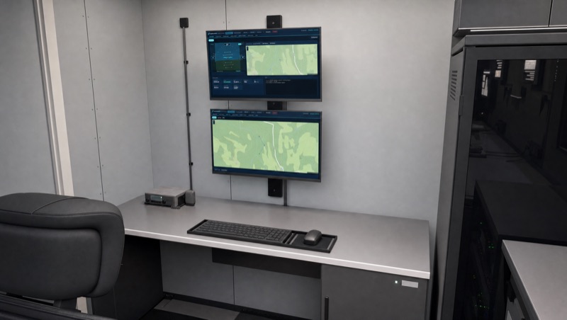 Ground control station at the far end of the container: two stacked monitors showing the DropForce ground control software, desk, seat and server rack.